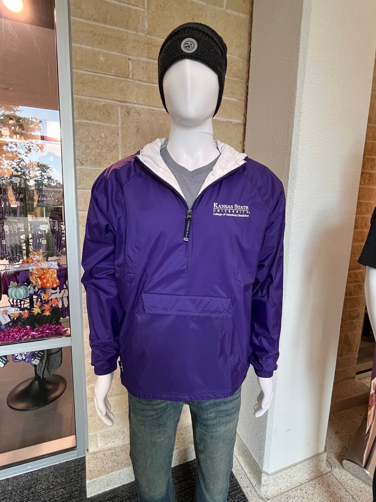 Mannequin wearing a purple rain jacket with a white CVM logo, standing on a tiled floor.