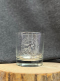 Clear old fashion glass with the CVM seal logo in the center, on a wooden surface and gray background.