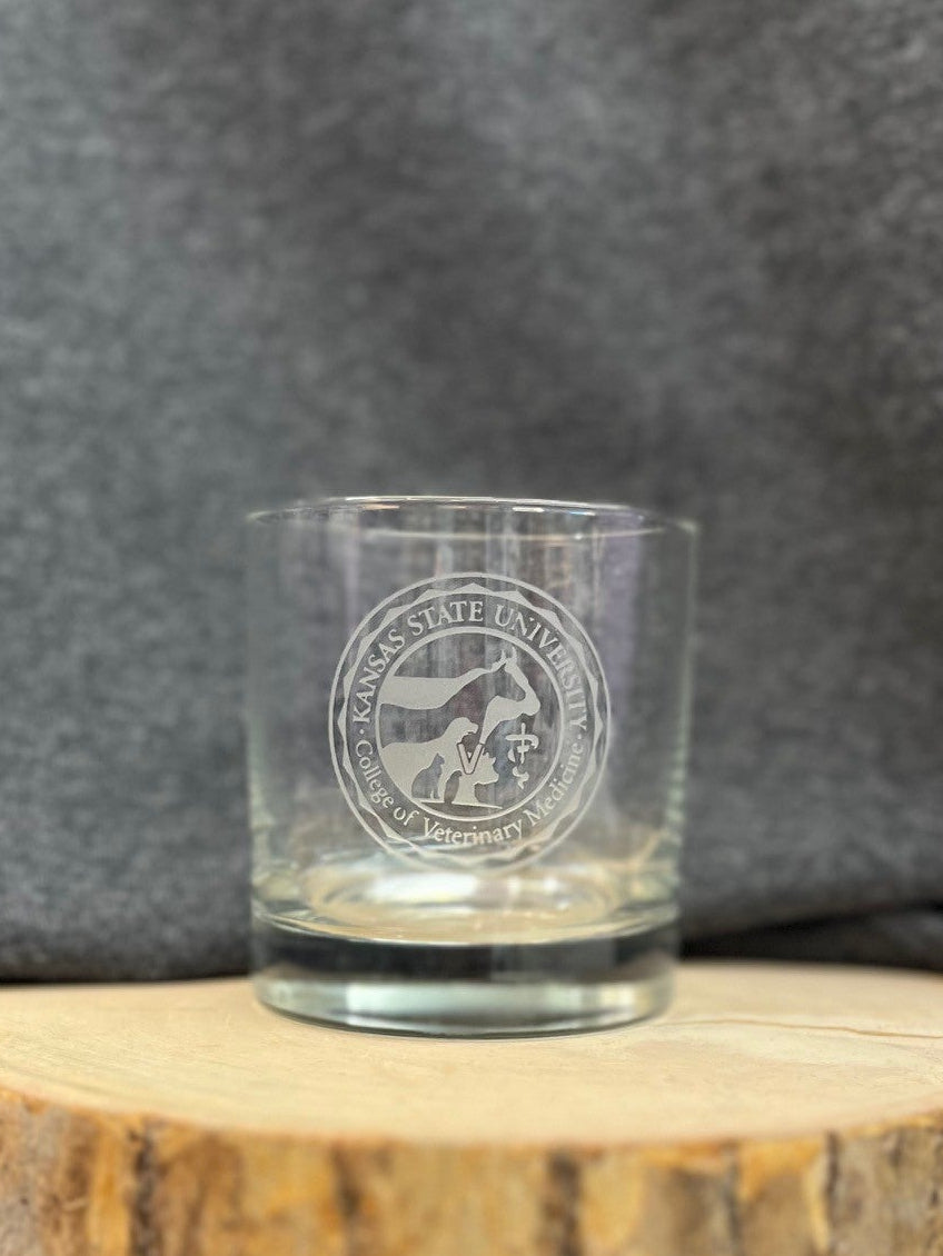 Clear old fashion glass with the CVM seal logo in the center, on a wooden surface and gray background.