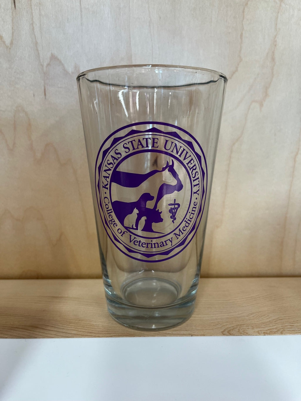 A clear pint glass with a purple Kansas State University College of Veterinary Medicine logo in center.  