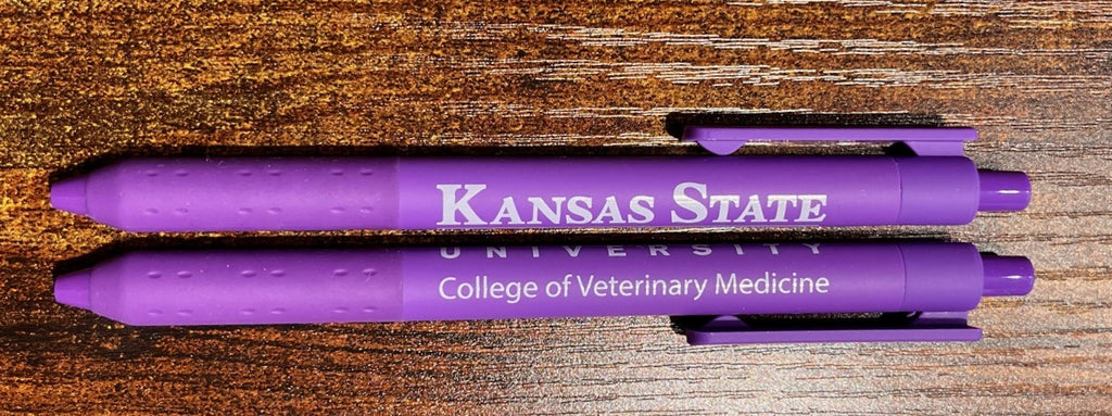 Two purple pens with 'Kansas State University College of Veterinary Medicine' text on a wooden surface