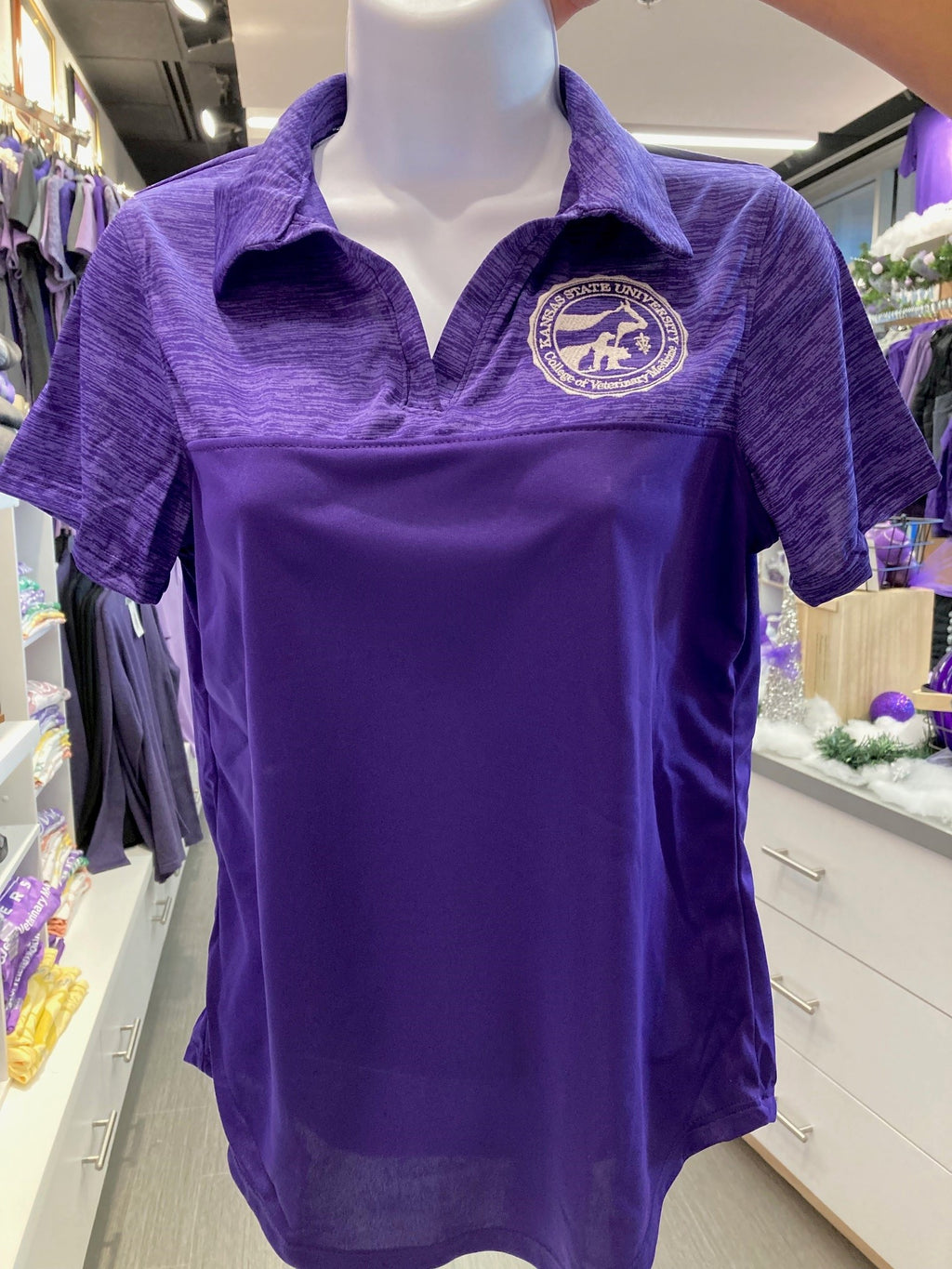 A purple Augusta sport shirt for ladies displayed on a mannequin, featuring a collar and short sleeves with the CVM seal on the chest.