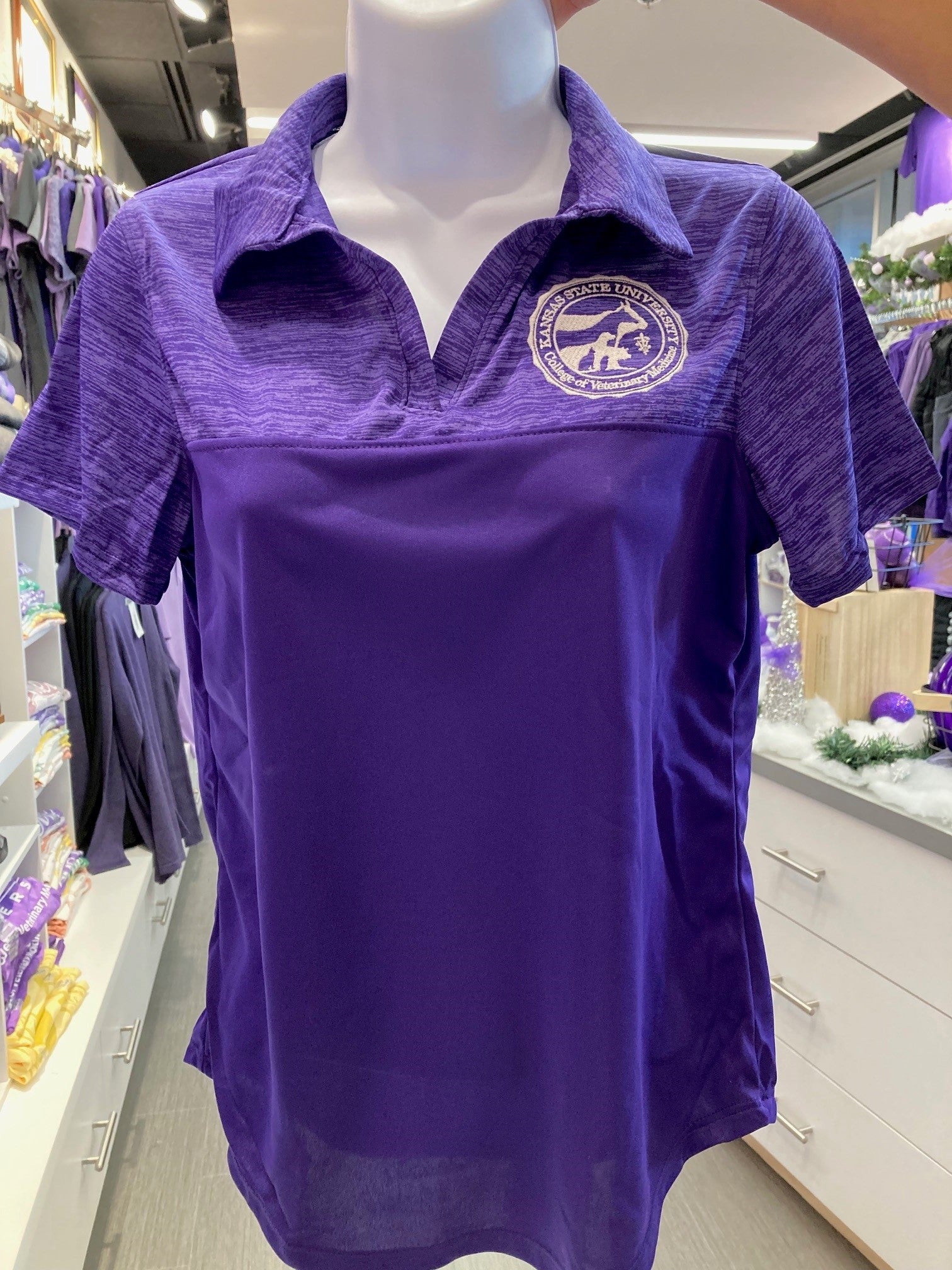 A purple Augusta sport shirt for ladies displayed on a mannequin, featuring a collar and short sleeves with the CVM seal on the chest.
