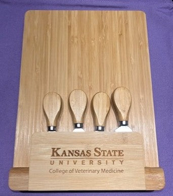 Bamboo cutting board with four wooden cheese knives and engraved "Kansas State University College of Veterinary Medicine" text on a purple background