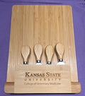 Bamboo cutting board with four wooden cheese knives and engraved "Kansas State University College of Veterinary Medicine" text on a purple background