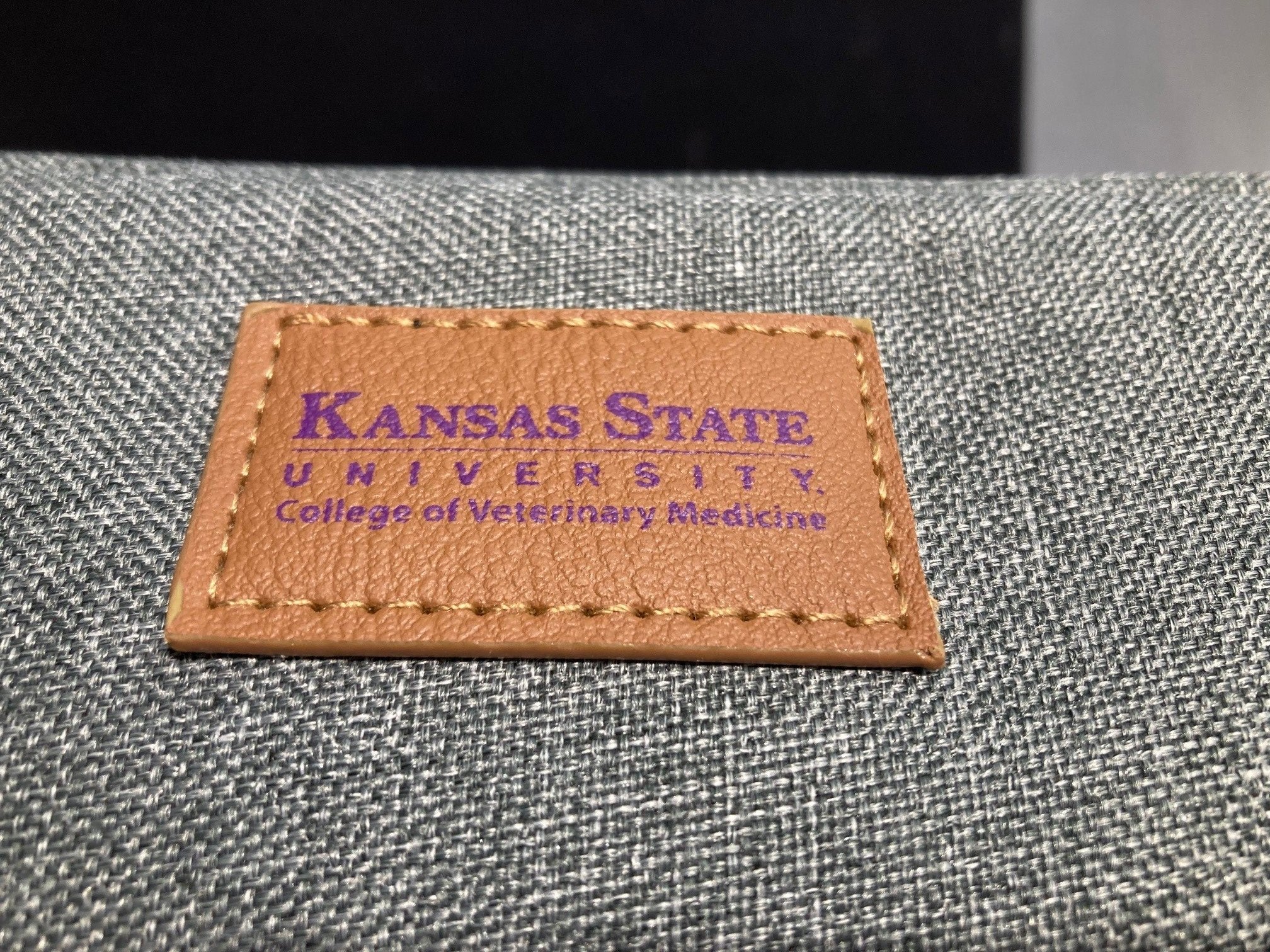 A close-up of the brown leather label that reads 'Kansas State University College of Veterinary Medicine'.