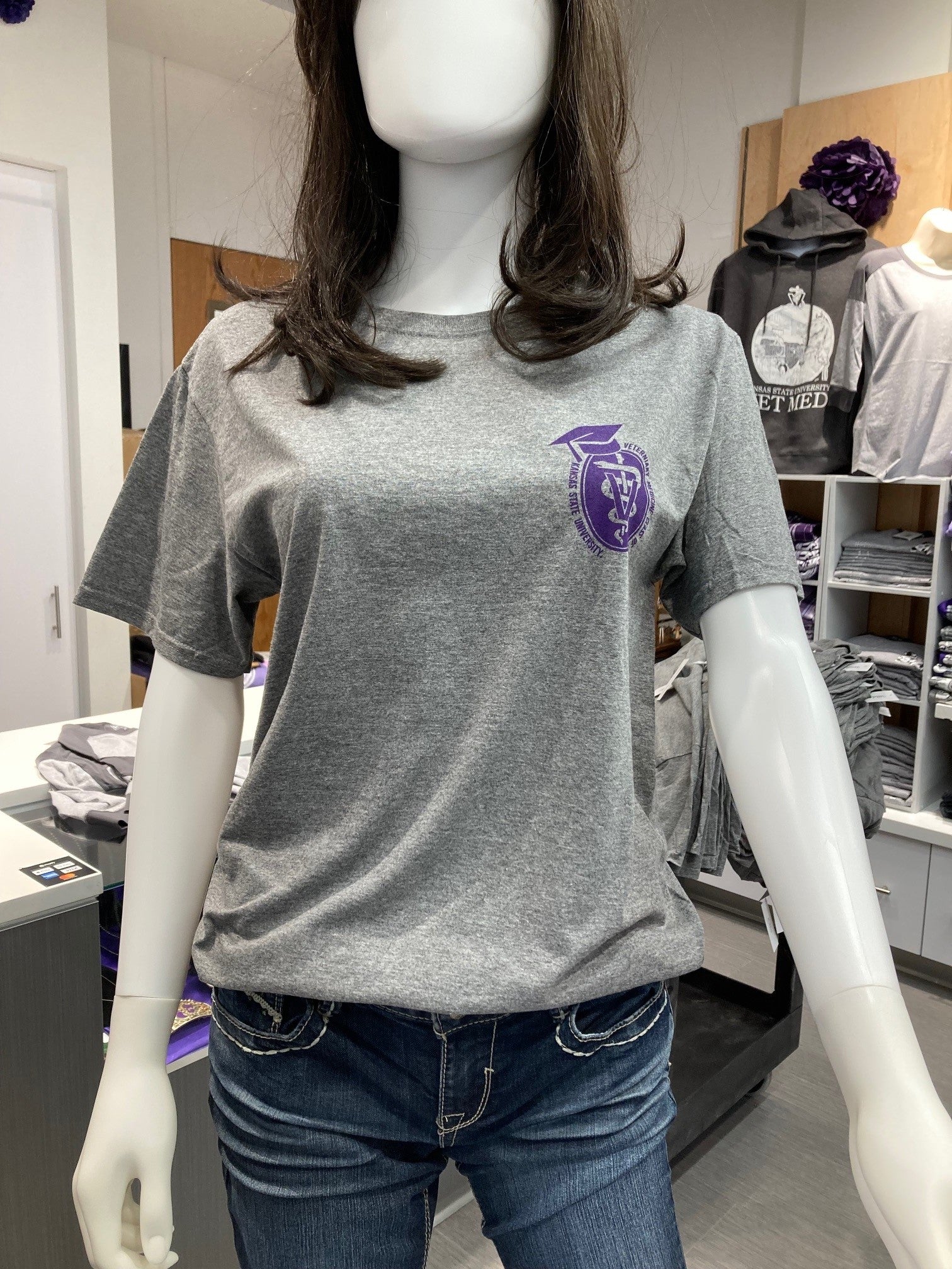 A gray t-shirt with a purple graduation emblem on the left chest area, displayed on a mannequin.