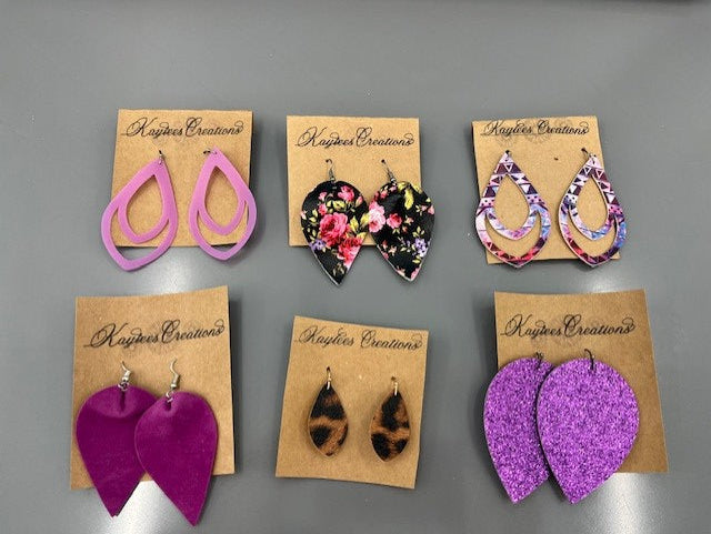 A variety of colorful Kaylee's Creations earrings on branded cards against a gray background.