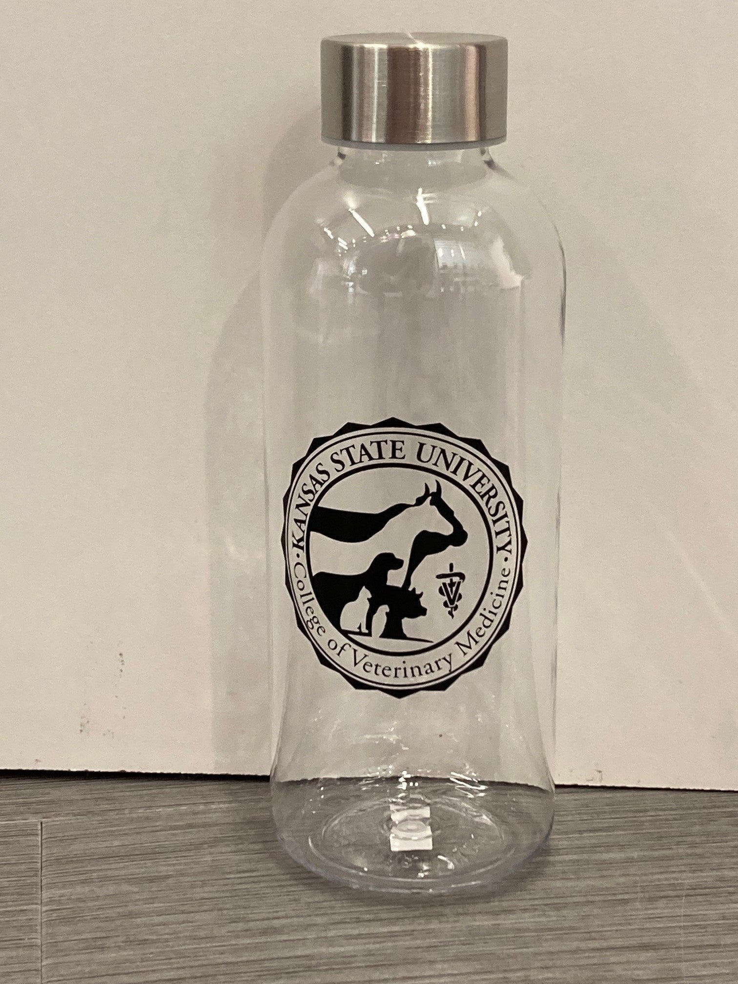 A clear plastic water bottle with a metal screw cap, featuring a black and white CVM seal. 
