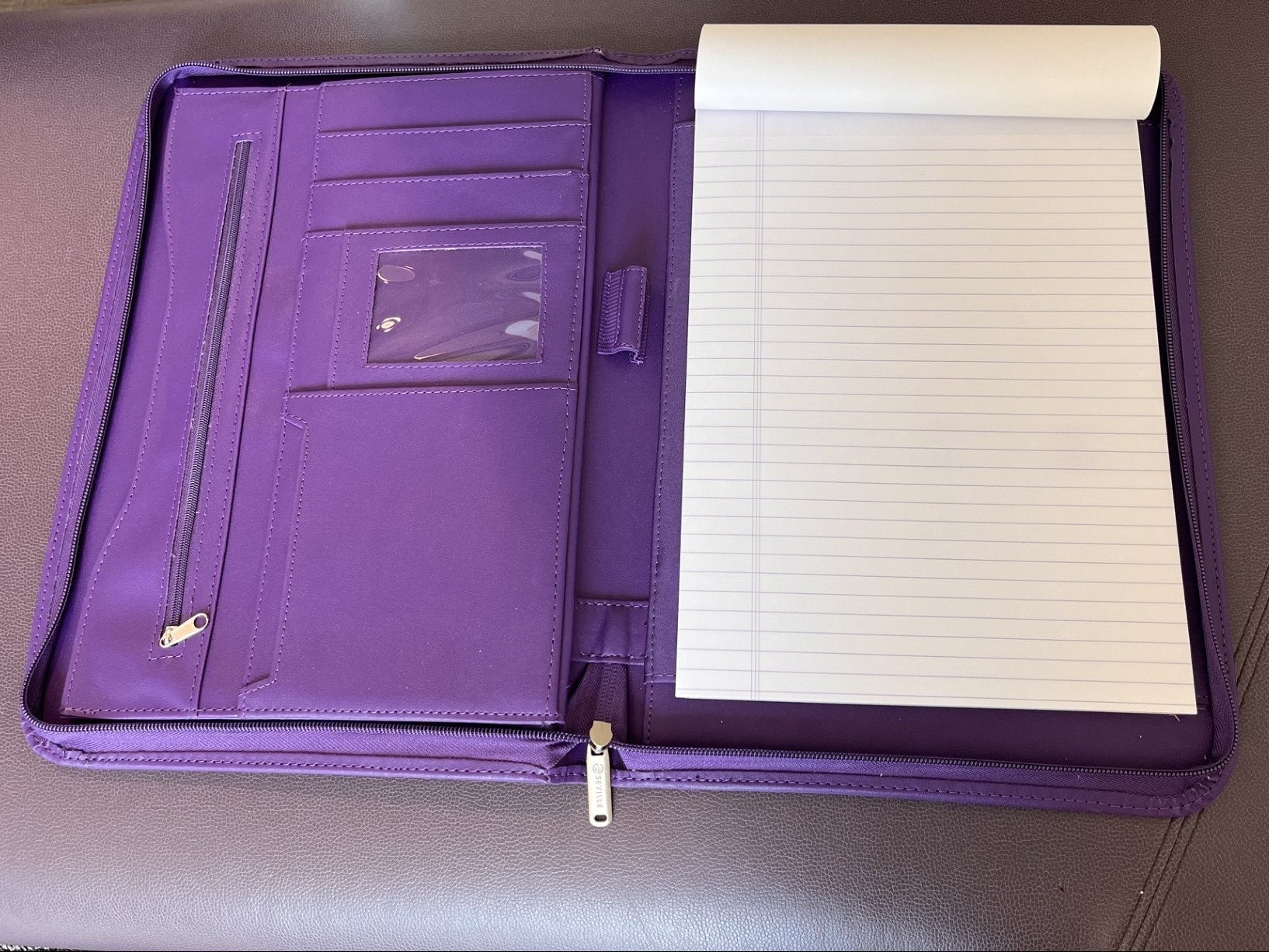 Purple zippered portfolio folder with multiple interior card slots, a clear ID window, and a lined notepad partially unfolded