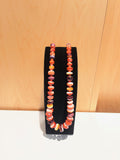 Orange, yellow, red and purple colored oyster beaded necklace on a black stand against a wooden background. 