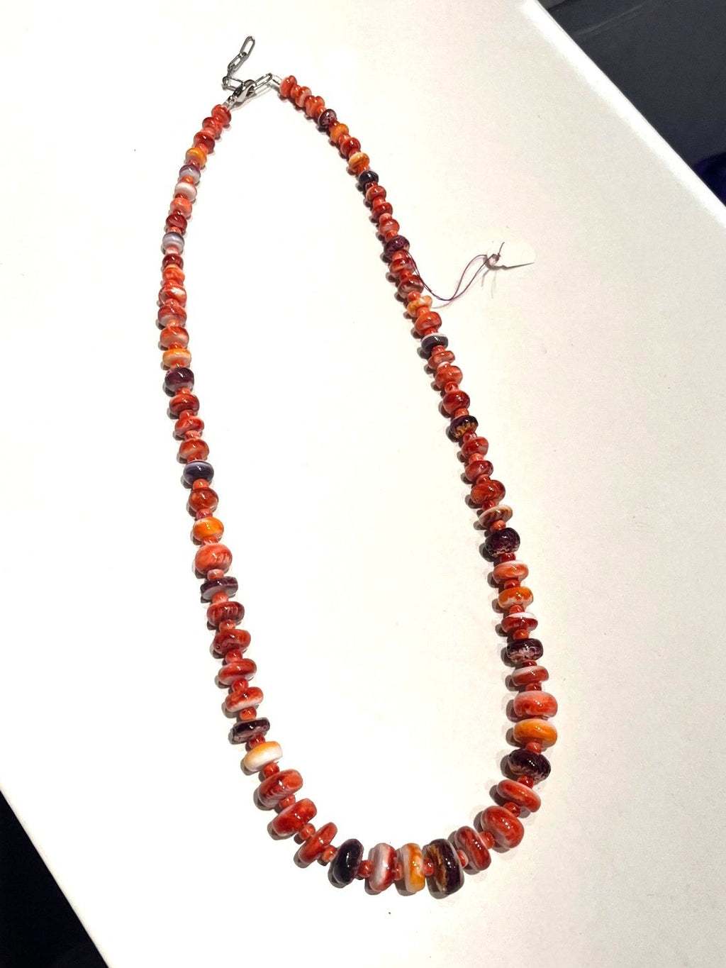 Orange, yellow, red and purple colored oyster beaded necklace against a white background. 