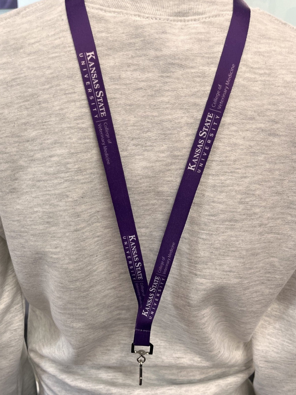 A person wearing a light gray sweatshirt, wearing a purple Kansas State University lanyard with a key ring and keychain.