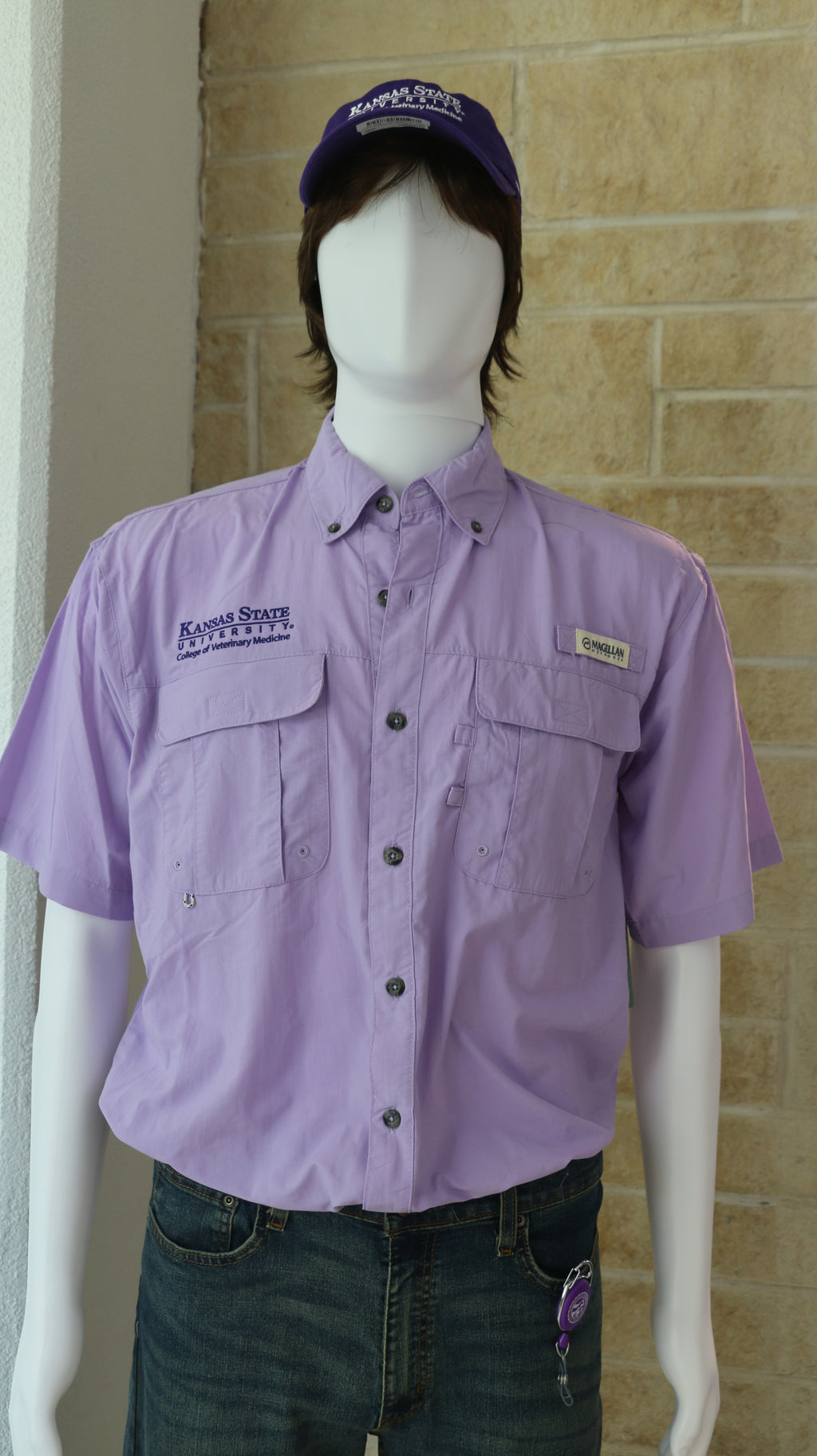 A mannequin wearing a short-sleeved purple colored fishing shirt with button-up collar and the Magellan Outdoors logo. It also has a purple K-State CVM logo on the upper right chest area. 