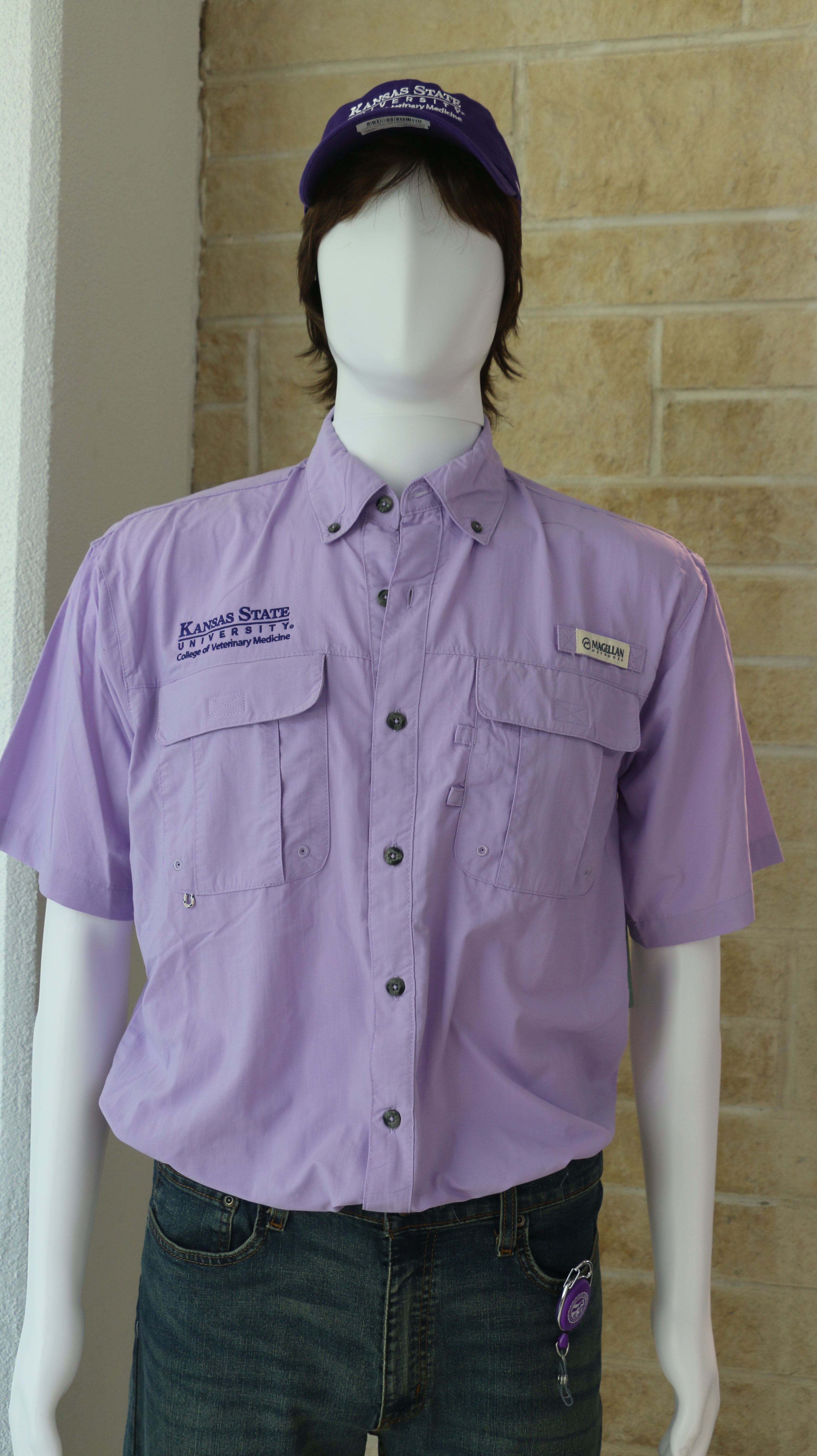 A mannequin wearing a short-sleeved purple colored fishing shirt with button-up collar and the Magellan Outdoors logo. It also has a purple K-State CVM logo on the upper right chest area. 