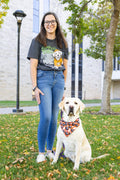 A person standing next to a seated dog, wearing a heathered black t-shirt with a graphic of a dog in training in a Halloween theme.
