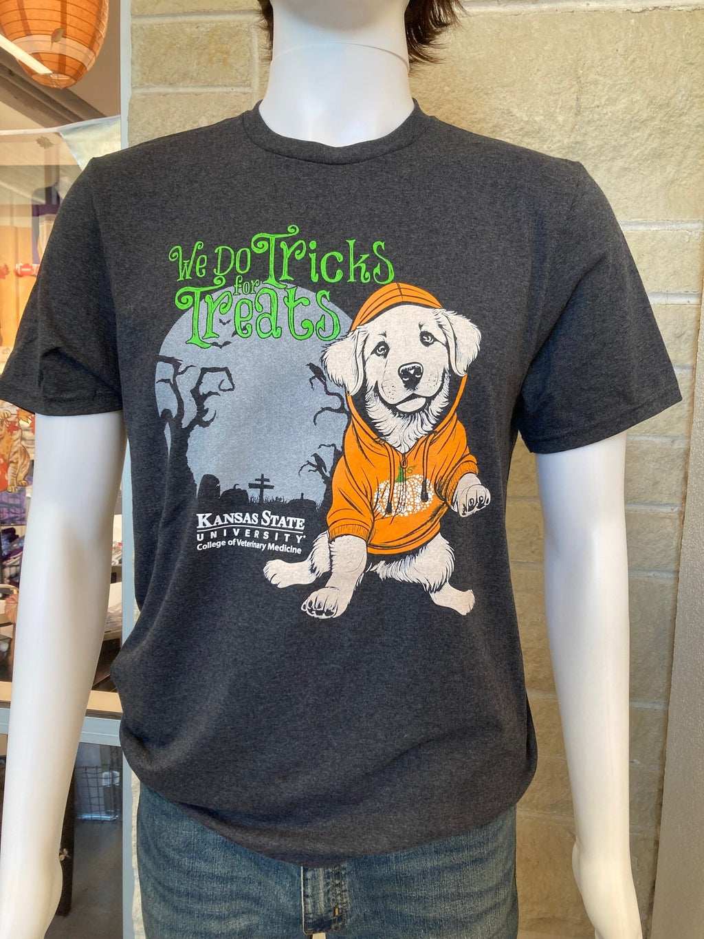 A black heather t-shirt featuring a dog with an orange hoodie design and the text 'We do Tricks for Treats' on the front. There is also a white K-State CVM logo at the bottom of the Halloween themed graphic. 