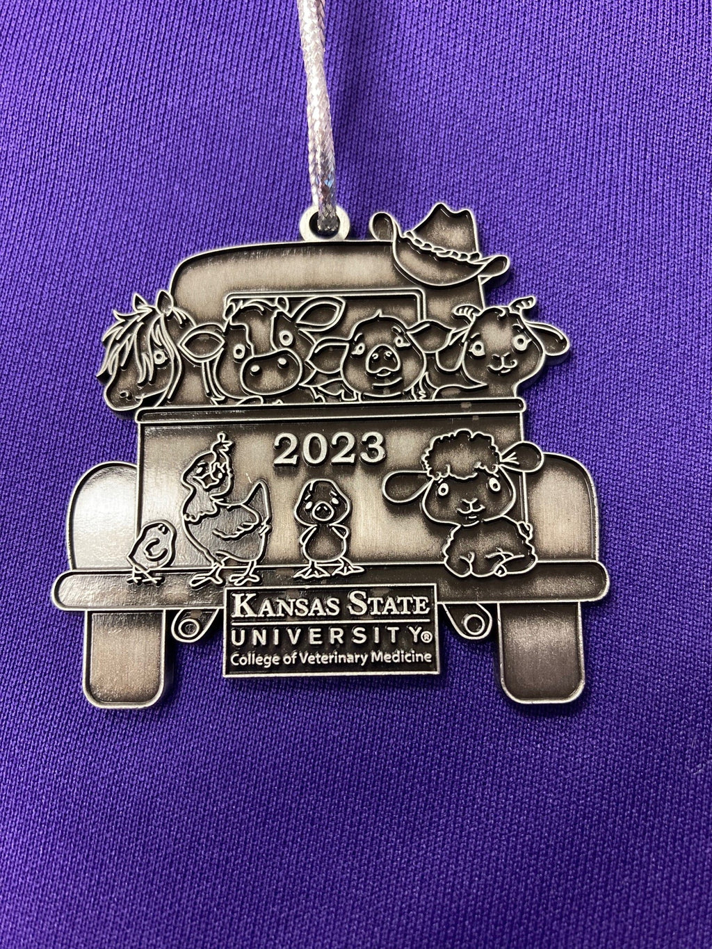 A pewter Christmas ornament with a vintage truck design with '2023' and 'Kansas State University' text on it.