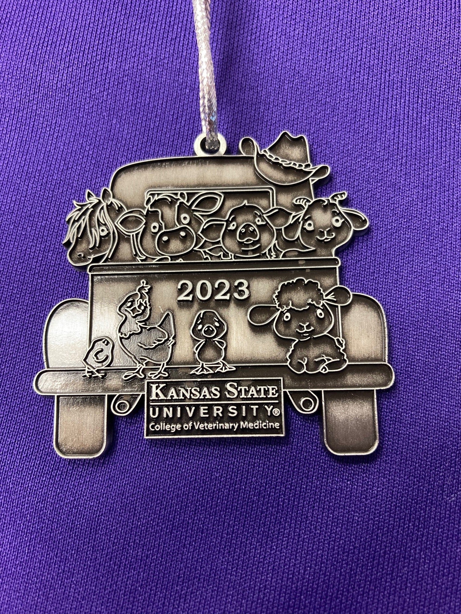 A pewter Christmas ornament with a vintage truck design with '2023' and 'Kansas State University' text on it.