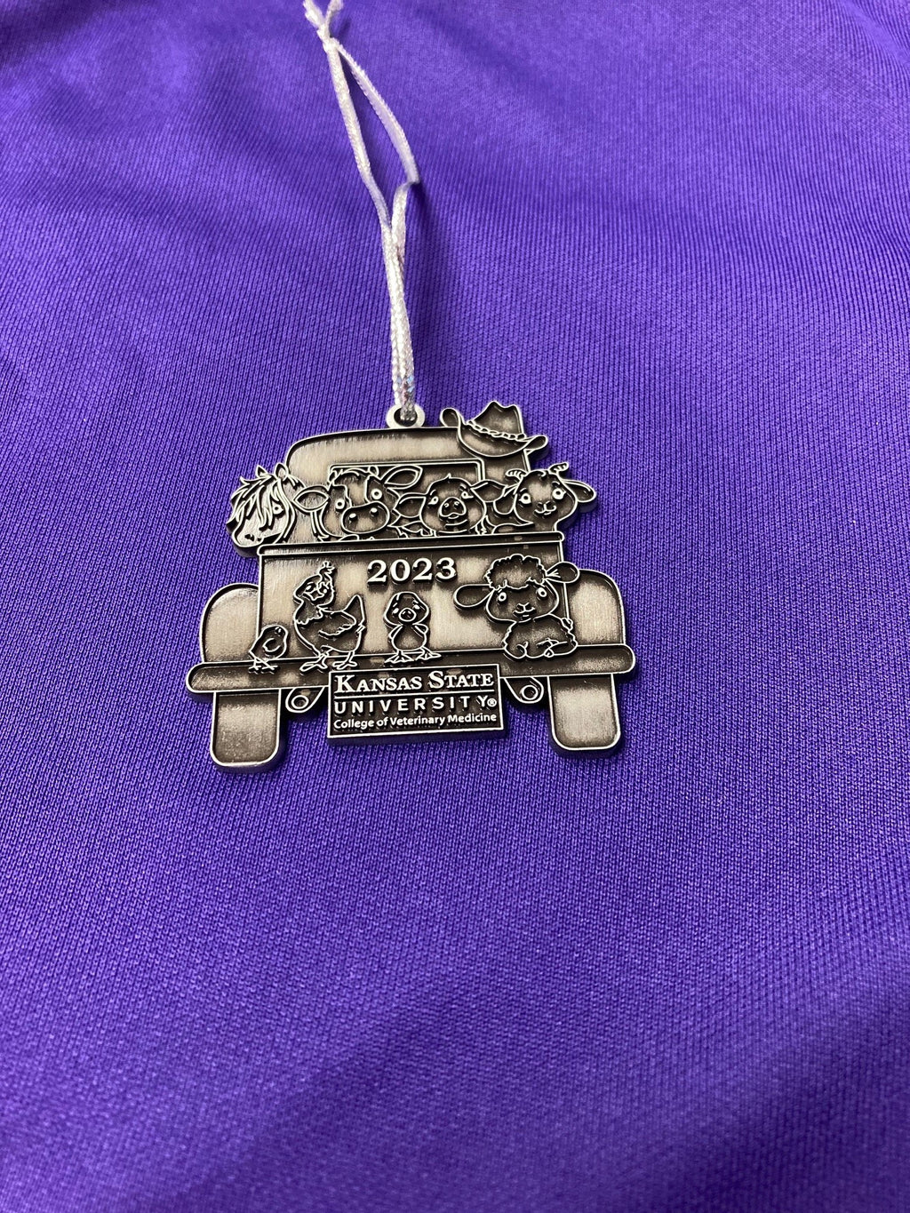 A pewter Christmas ornament with a vintage truck design with '2023' and 'Kansas State University' text on it.
