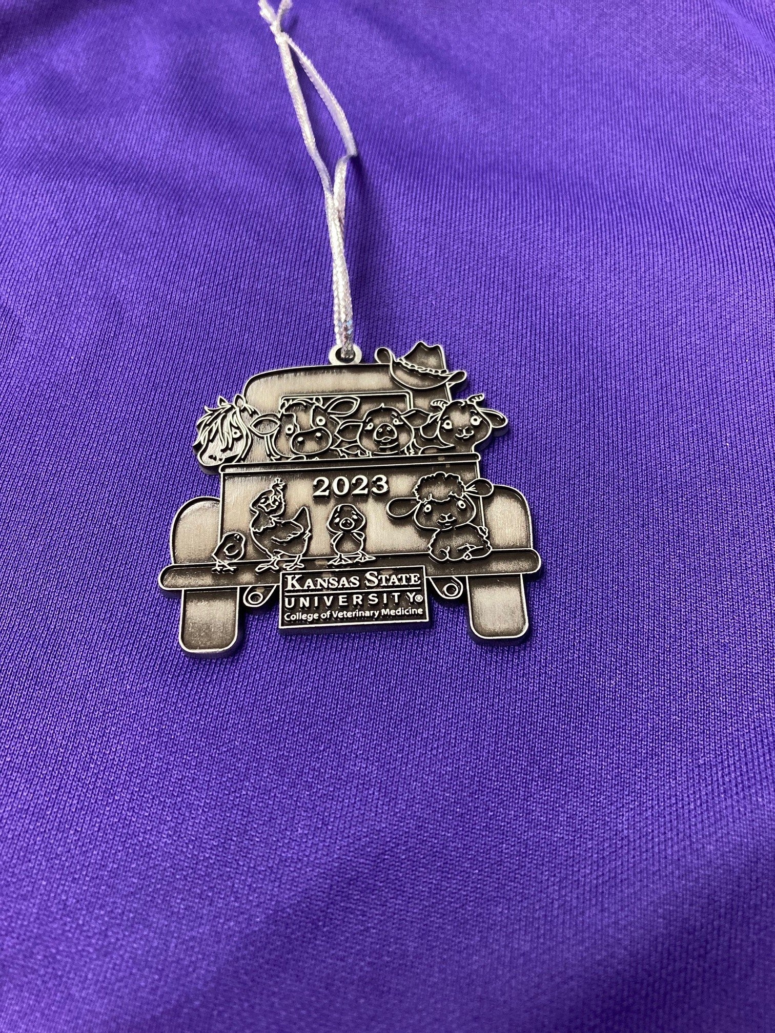 A pewter Christmas ornament with a vintage truck design with '2023' and 'Kansas State University' text on it.