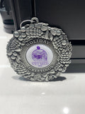 A pewter 2024 Christmas ornament with the text "Holiday Greetings" around a circular center that has an animal image and the text "Kansas State University Vet Med 2024" on a white background. 