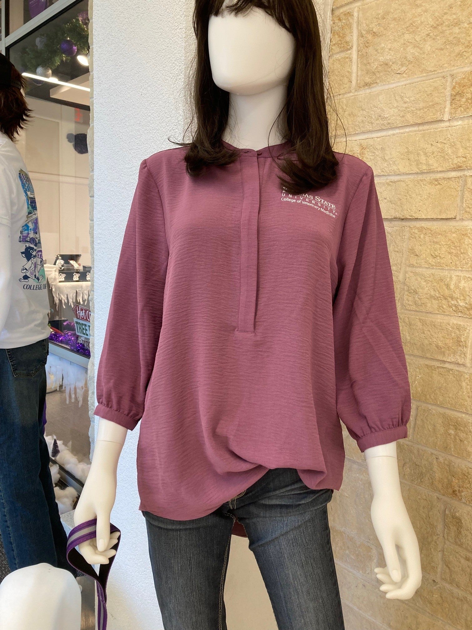 A mannequin displaying a purple 3/4 sleeve tunic with a round neckline, half button up option, a white K-State CVM logo on the left chest, and textured fabric.