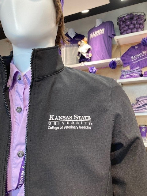 A mannequin wearing a black Port Authority Collective Soft Shell Jacket with a collar and white K-State CVM logo, displayed in a retail setting.