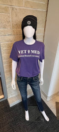 Mannequin wearing a purple 'Vet Med' shirt with Kansas State University text, standing against a brick wall.