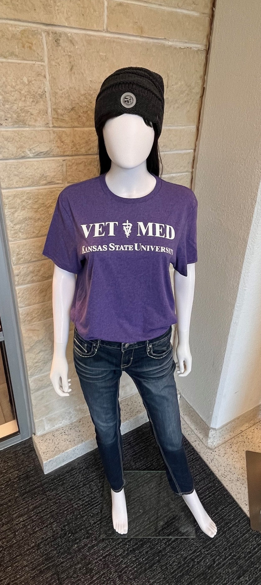 Mannequin wearing a purple 'Vet Med' shirt with Kansas State University text, standing against a brick wall.