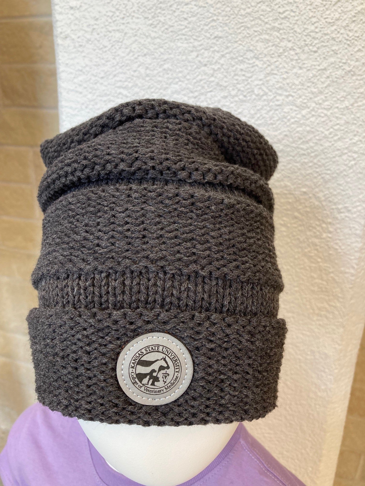 A gray knit beanie with a CVM seal patch on the front displayed on a mannequin head.