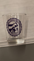 A clear 1.5oz shot glass with a purple custom CVM seal printed on it.