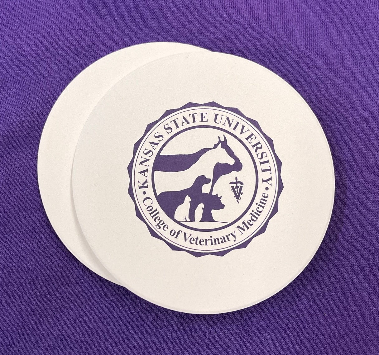 Round coaster with Kansas State University College of Veterinary Medicine seal in dark purple against a white background color.