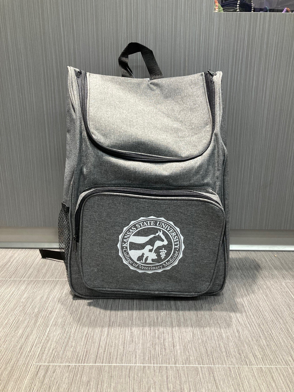 A gray Trek backpack with a front pocket and a white CVM seal. 