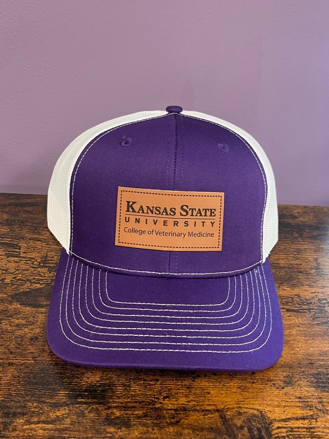 Purple and white trucker hat with Kansas State University wordmark logo on leather patch. 