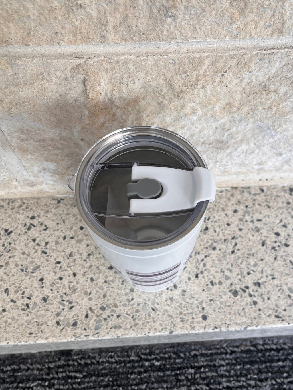 A top view of the white tumbler with a clear lid on a stone surface. 
