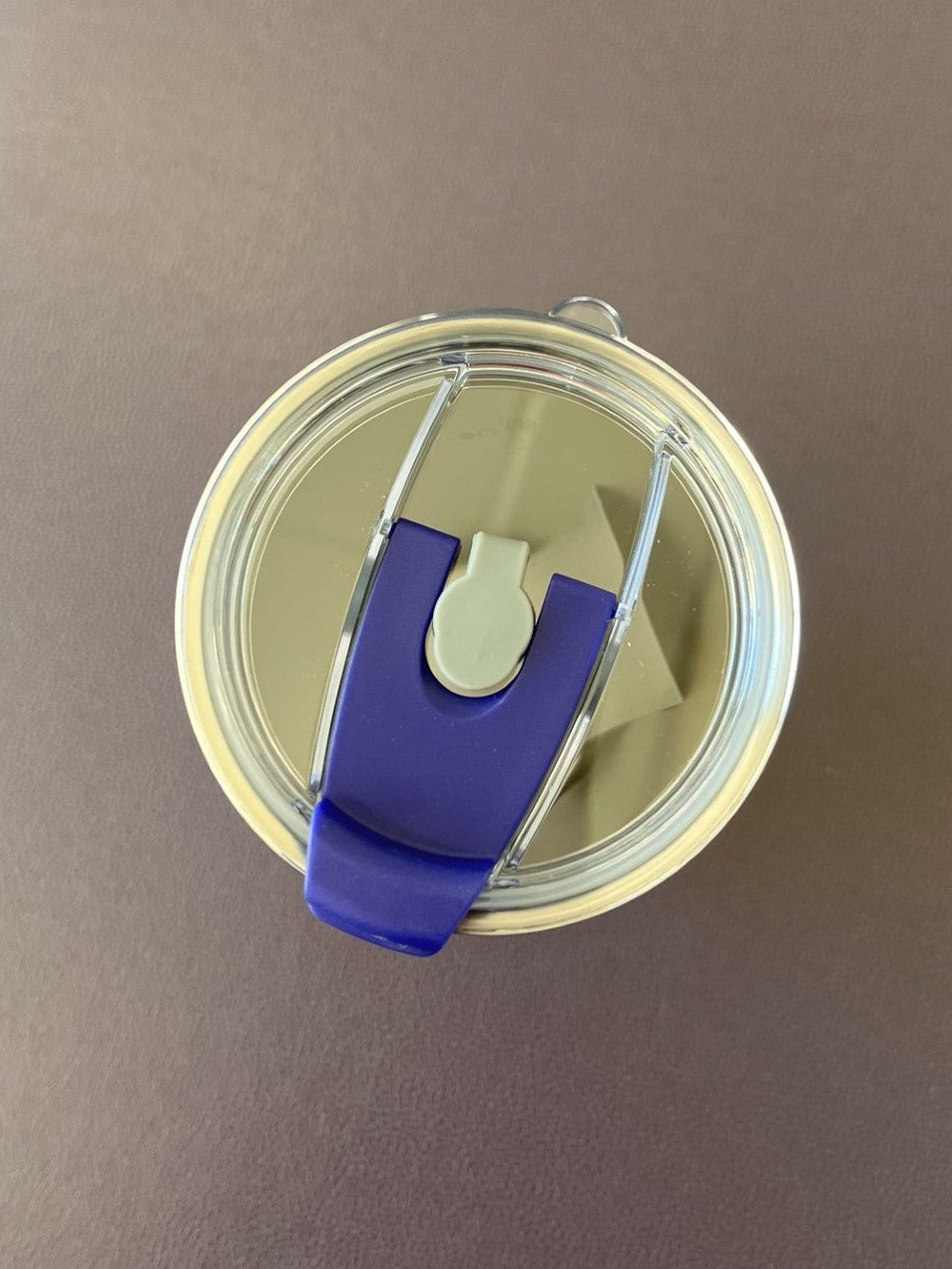 Top-down view of a clear travel tumbler with a purple flip-straw lid, resting on a brown leather surface.