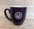 A purple ceramic coffee mug with a white printed seal of the College of Veterinary Medicine on the front, resting on a speckled stone countertop against a matching stone backsplash.