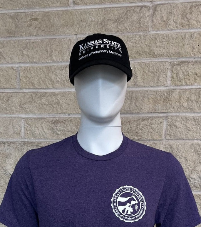 A mannequin wearing a dark purple heathered t-shirt with a white circular graphic on the left chest, paired with  a black baseball cap, set against a beige brick wall background.