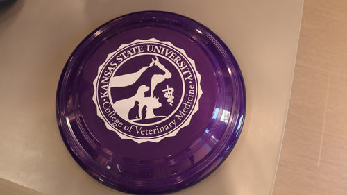 A purple frisbee with the white seal of the College of Veterinary Medicine in the center. 