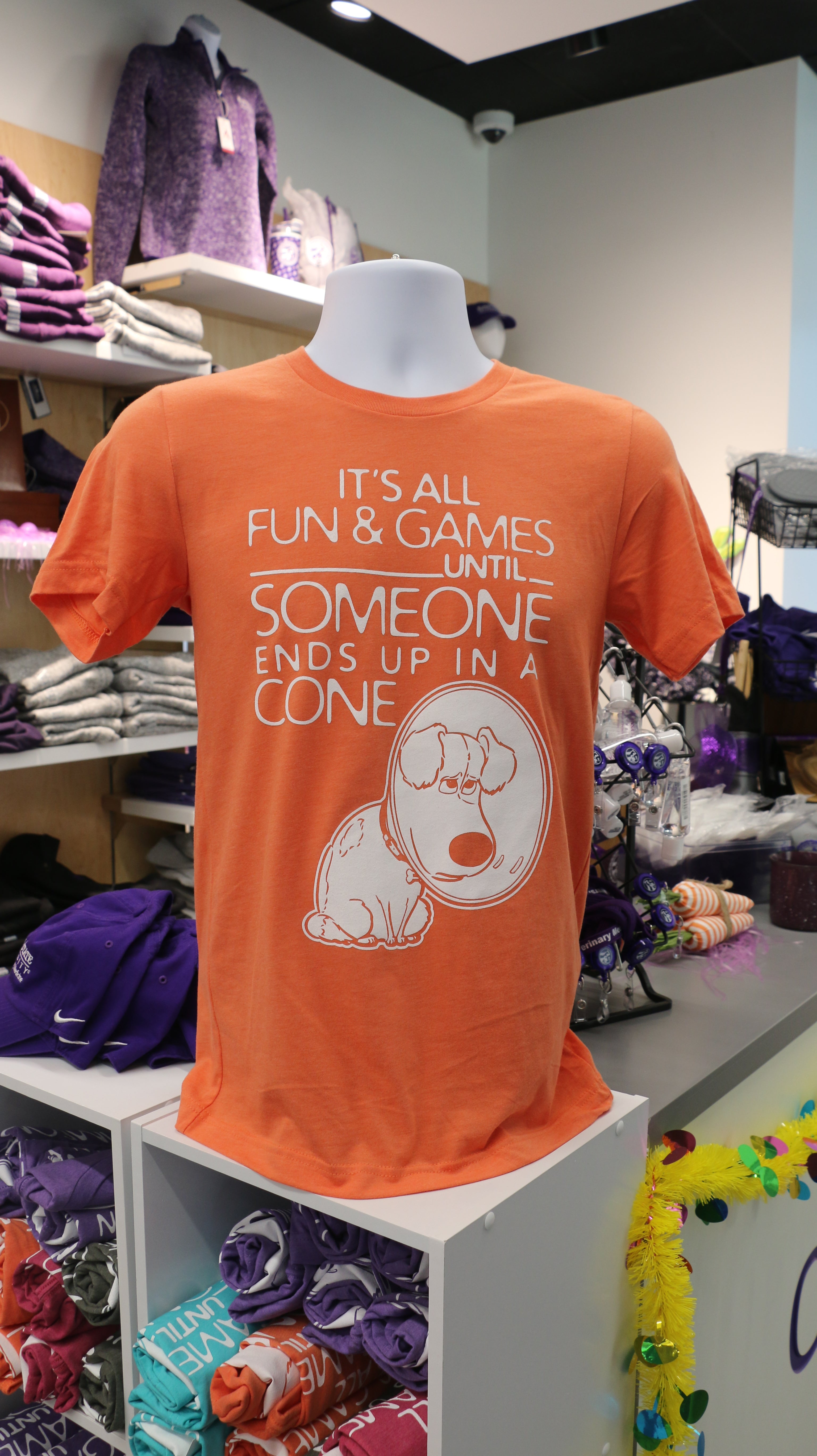 An orange Bella Canvas t-shirt with white text reading "It's all fun & games until SOMEONE ends up in a CONE" with a dog in a cone graphic design on it, displayed on a mannequin.