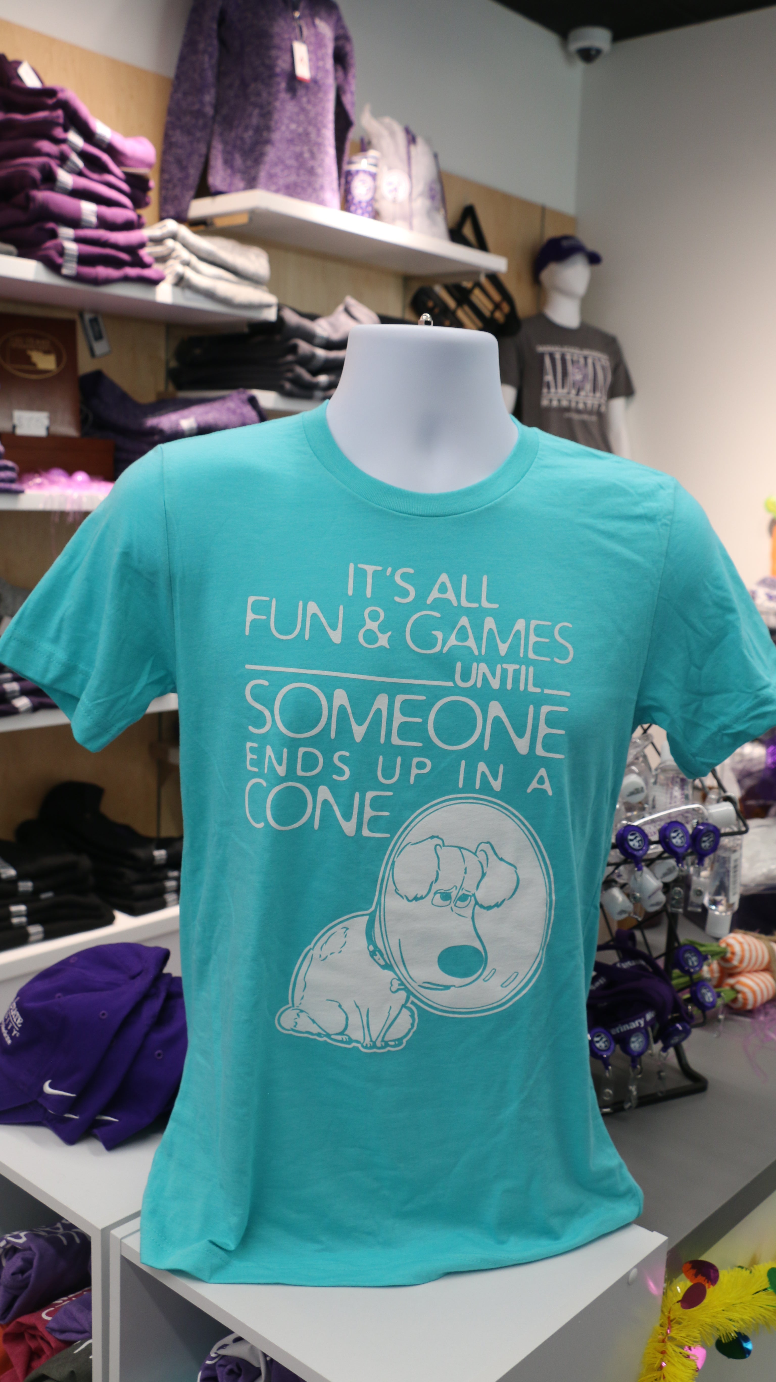 A bright baby blue Bella Canvas t-shirt with white text reading "It's all fun & games until SOMEONE ends up in a CONE" with a dog in a cone graphic design on it, displayed on a mannequin.