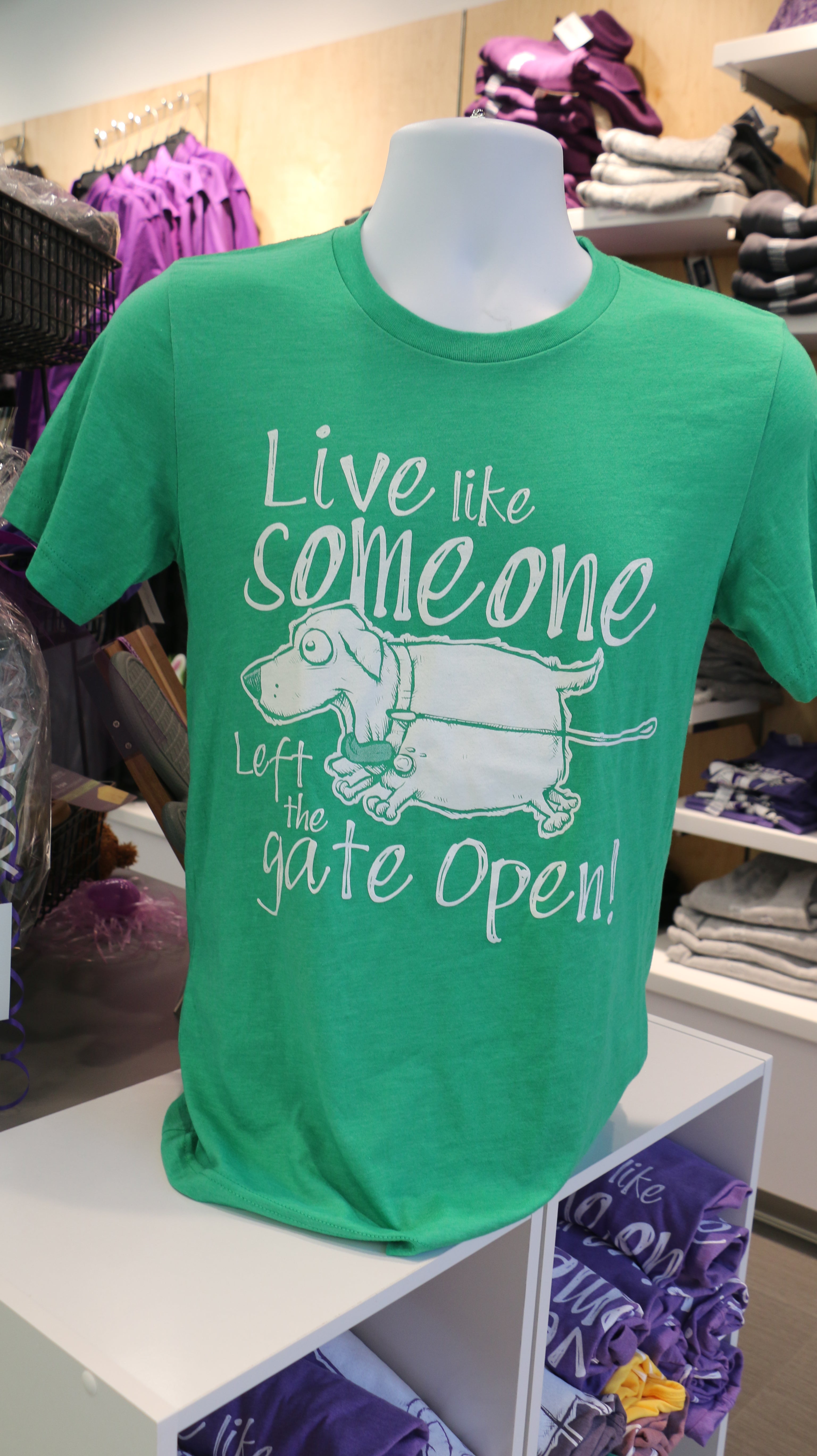 Green Bella Canvas t-shirt with white text that reads "Live like someone left the gate open!" with a dog illustration on the front.