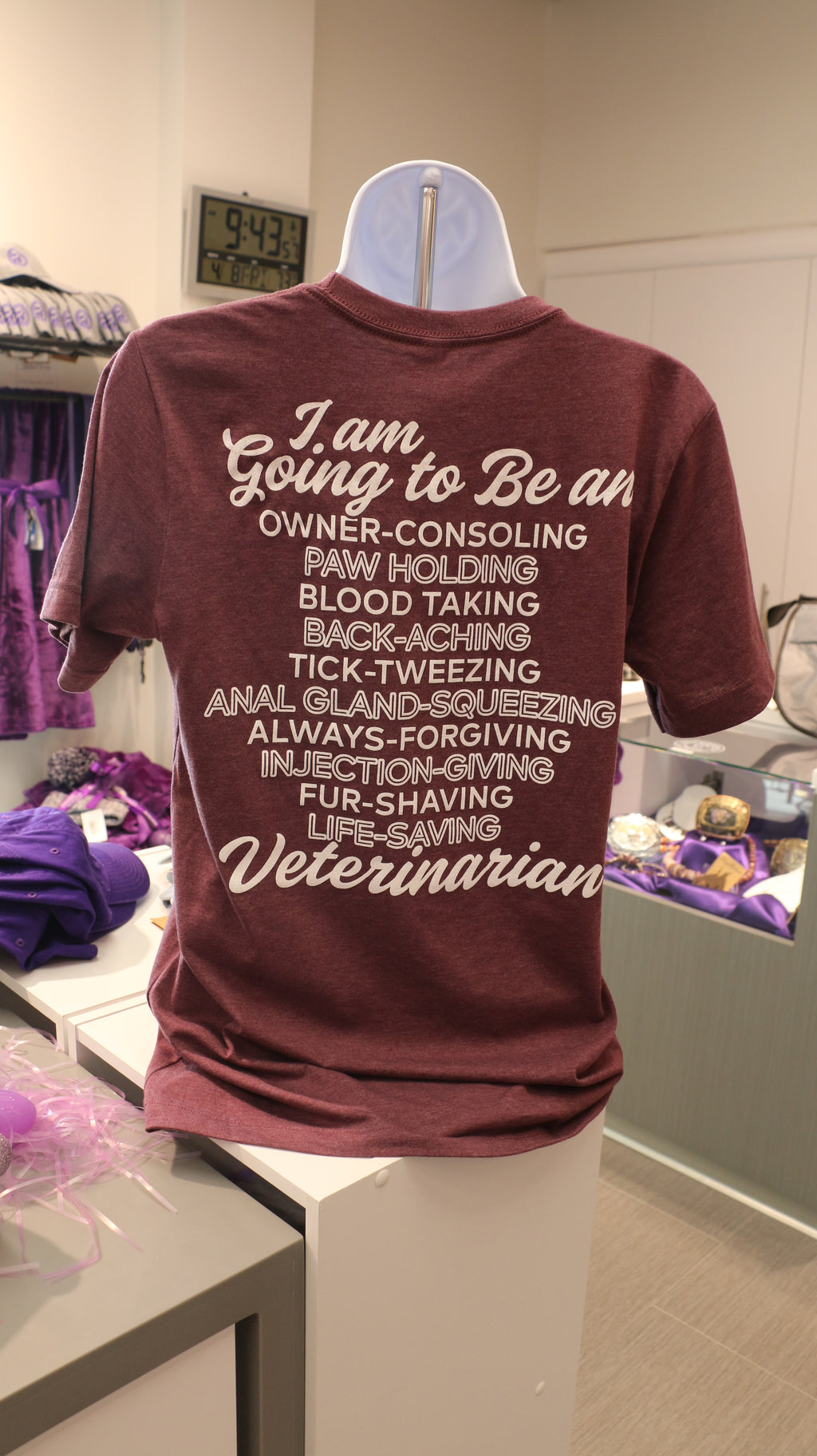 A rear view of the maroon Bella Canvas Vet T-shirt with white lettering that reads "I am going to be an owner-consoling, paw holding, blood taking, back-aching, tick-tweezing, anal gland-squeezing, always-forgiving, injection-giving, fur-shaving, life-saving Veterinarian" in cursive and print. 