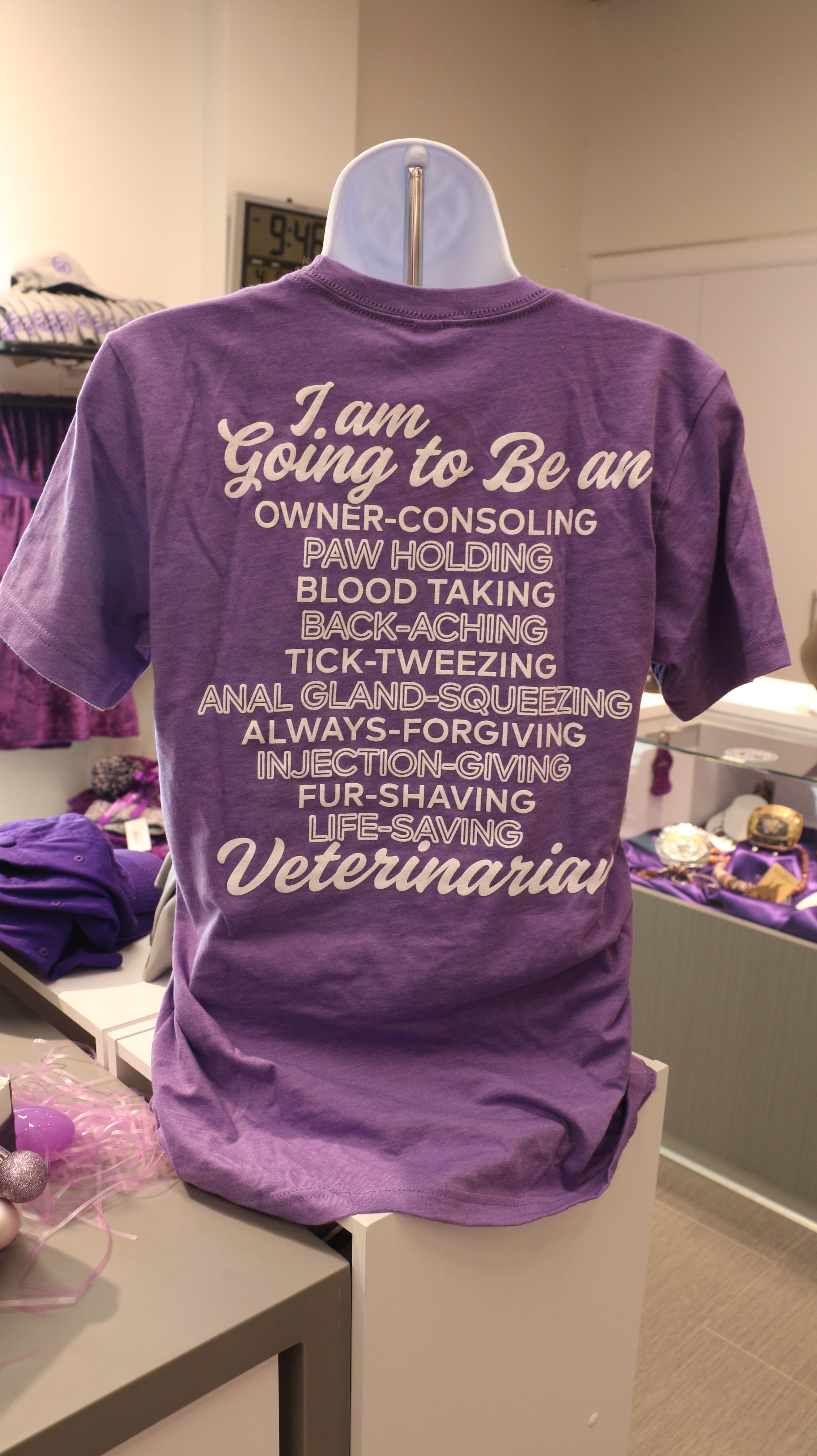 A rear view of the purple Bella Canvas Vet T-shirt with white lettering that reads "I am going to be an owner-consoling, paw holding, blood taking, back-aching, tick-tweezing, anal gland-squeezing, always-forgiving, injection-giving, fur-shaving, life-saving Veterinarian" in cursive and print. 