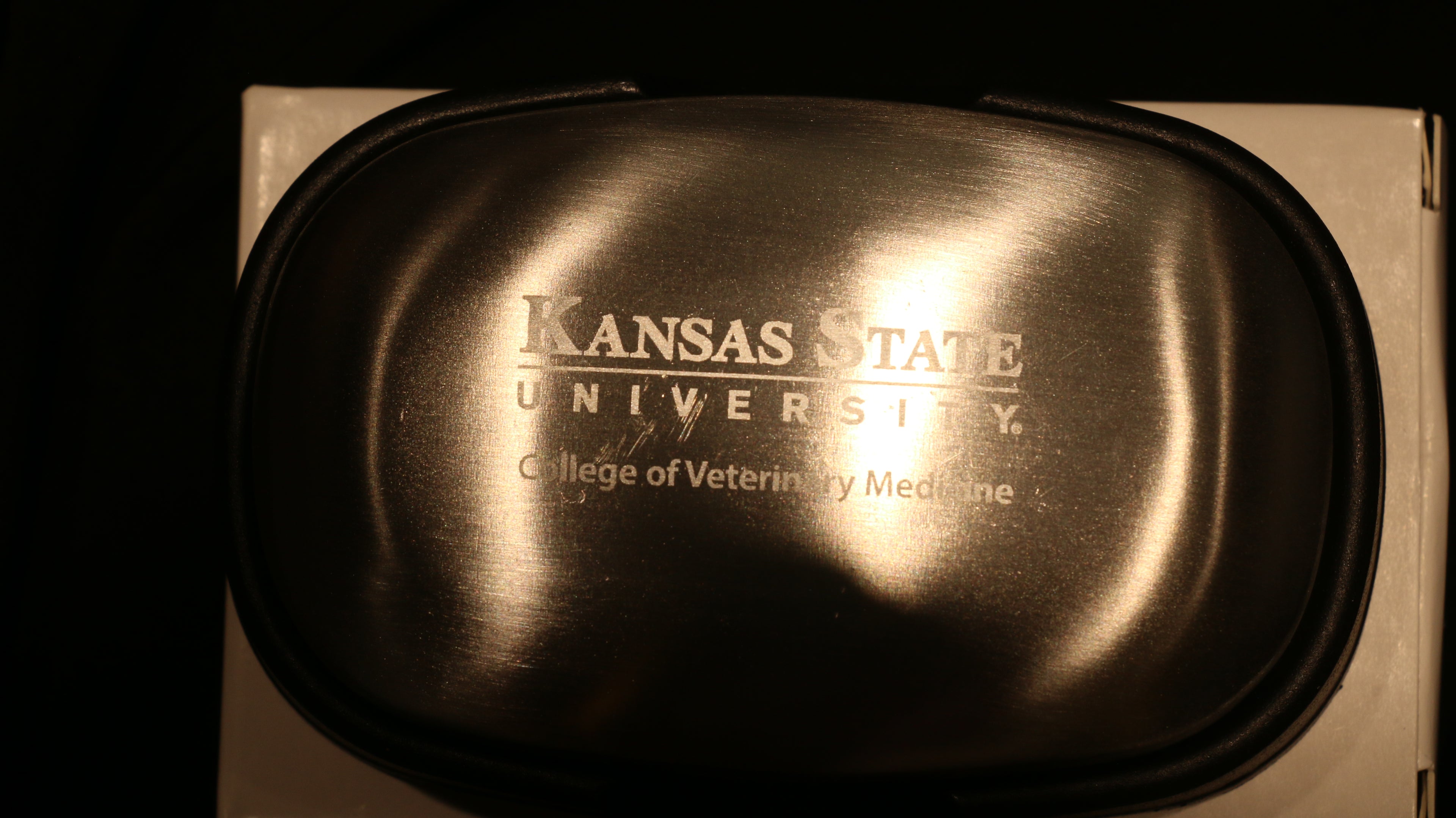 A silver steel soap bar packaged in a cardboard box with "Kansas State University College of Veterinary Medicine" engraved in the center. 
