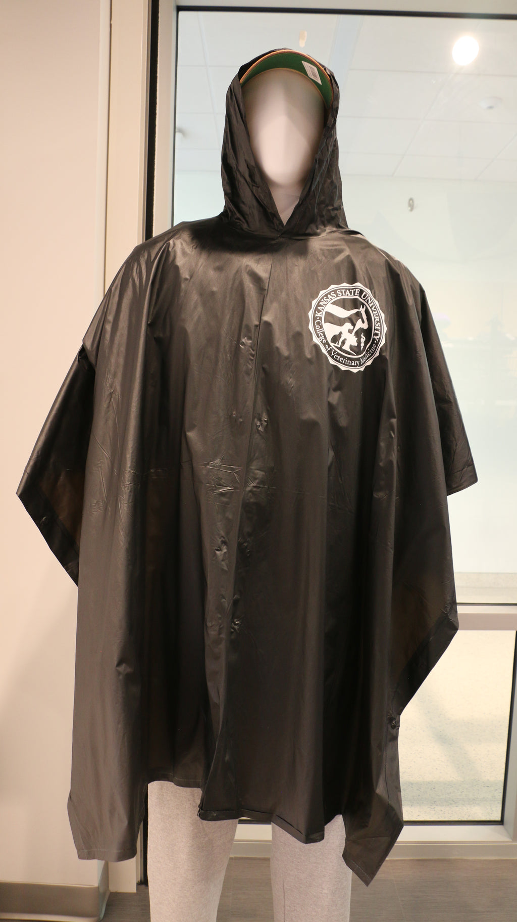 A black reusable buttoned poncho with a hood and white CVM logo on the upper left chest area. 