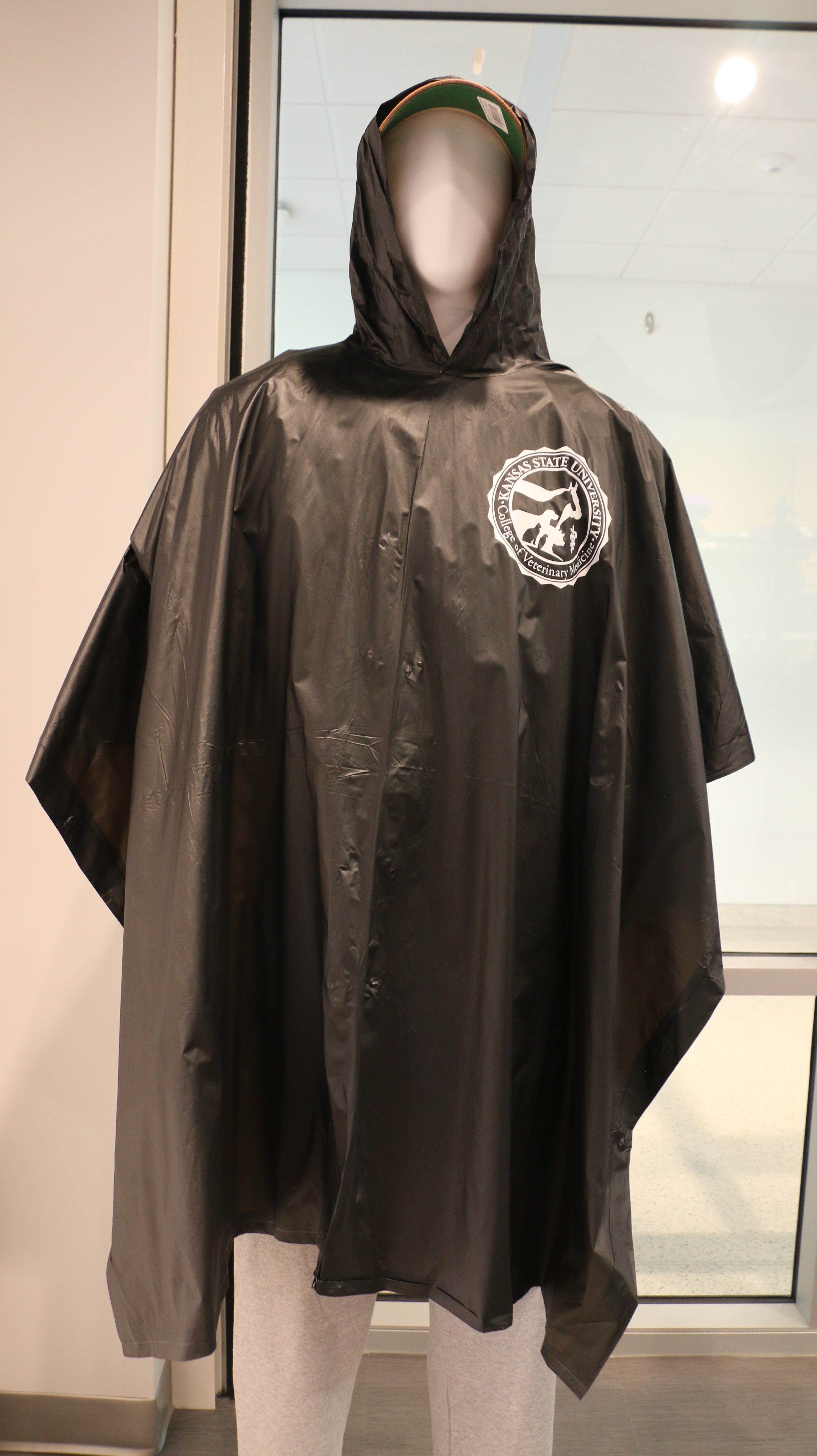 A black reusable buttoned poncho with a hood and white CVM logo on the upper left chest area. 