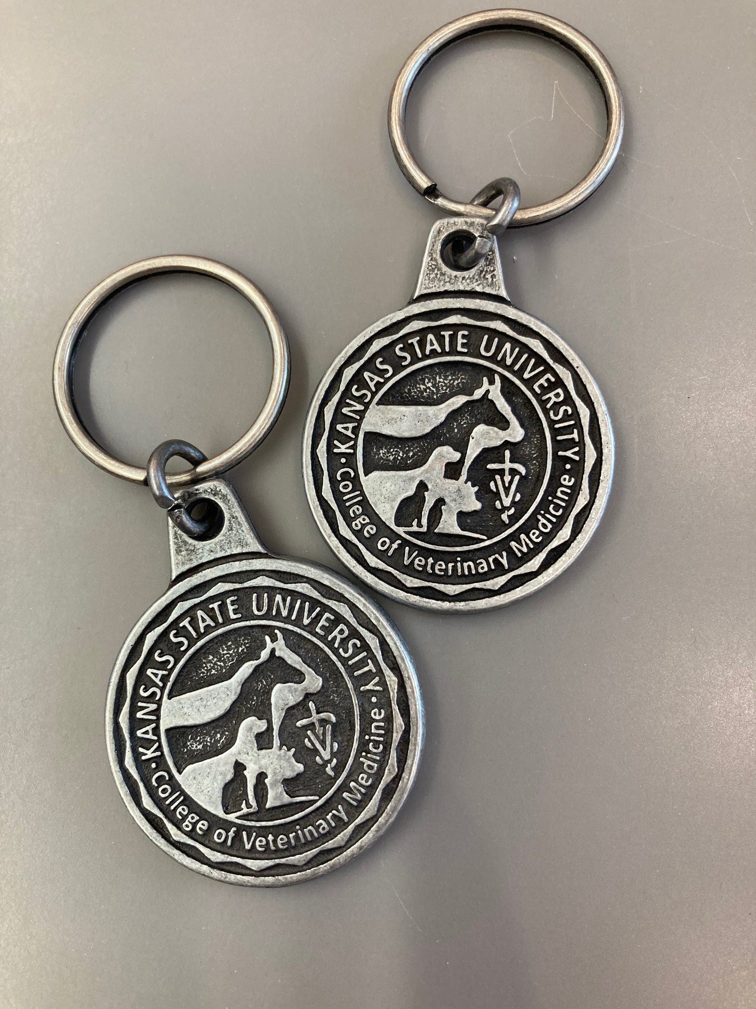 An image of two 1 3/8" diameter Antique style silver keychain customized with the College of Veterinary Medicine seal.