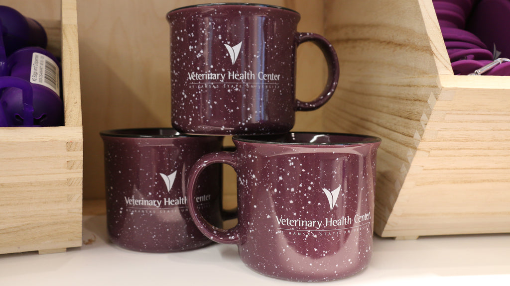 A set of three purple ceramic campfire mugs with white speckled patterns and the Veterinary Health Center logo printed on them, displayed on a shelf.